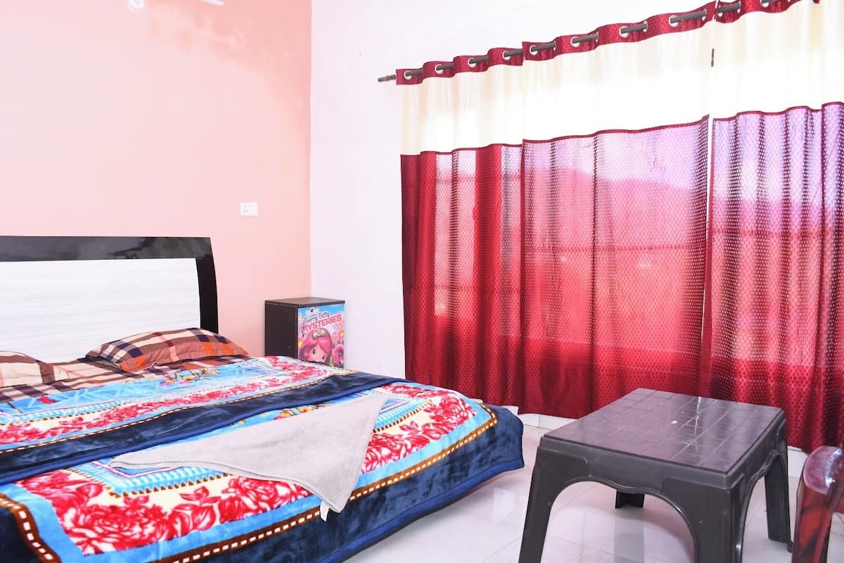 A bedroom with a bed, a bedside table, a chair, and a window with red curtains.