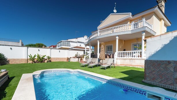 Una piscina con borde de azulejos, césped y un edificio con balcón.
