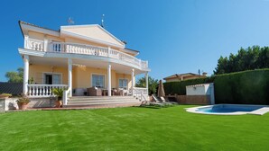 Una casa de dos pisos con un porche cubierto, una piscina y un césped bien cuidado.