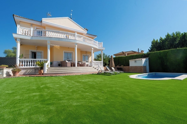 Una casa de dos pisos con un porche cubierto, una piscina y un césped bien cuidado.