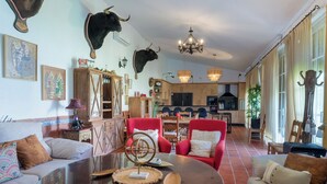 Una sala de estar con una mesa de centro de vidrio, sillas rojas y una cocina al fondo.