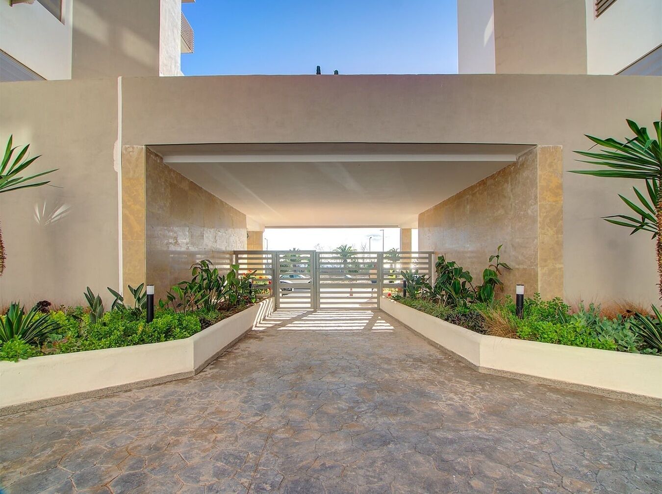 A modern building entrance with a stone floor, a metal gate, and green plants on either side.