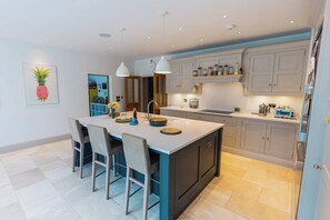 A modern kitchen with a central island, bar stools, pendant lighting, and a clock on the wall. - Large 6BR House near Goodwood, Garden & Parking (Chichester)