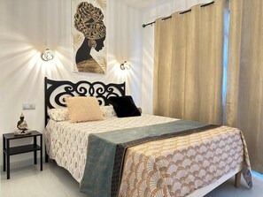 Une chambre à coucher comprenant un lit, une table de chevet, un luminaire fixé au mur et un rideau.