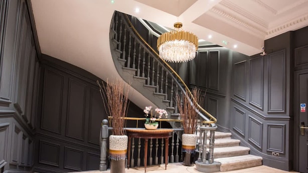 A grand staircase with a chandelier, dark wood paneling, and a round table with decorative items. - Chic Manchester Chinatown Stay Shops Nightlife (Manchester)