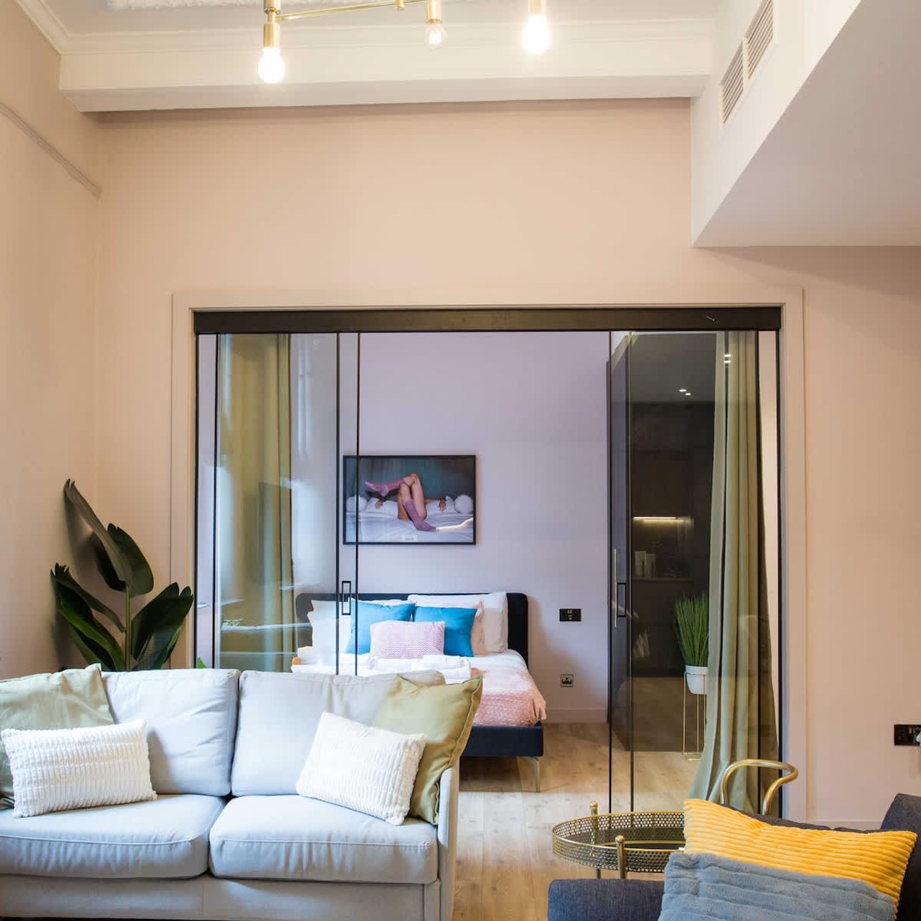 A modern living room with a sofa, a small table, and a bed with a glass partition.