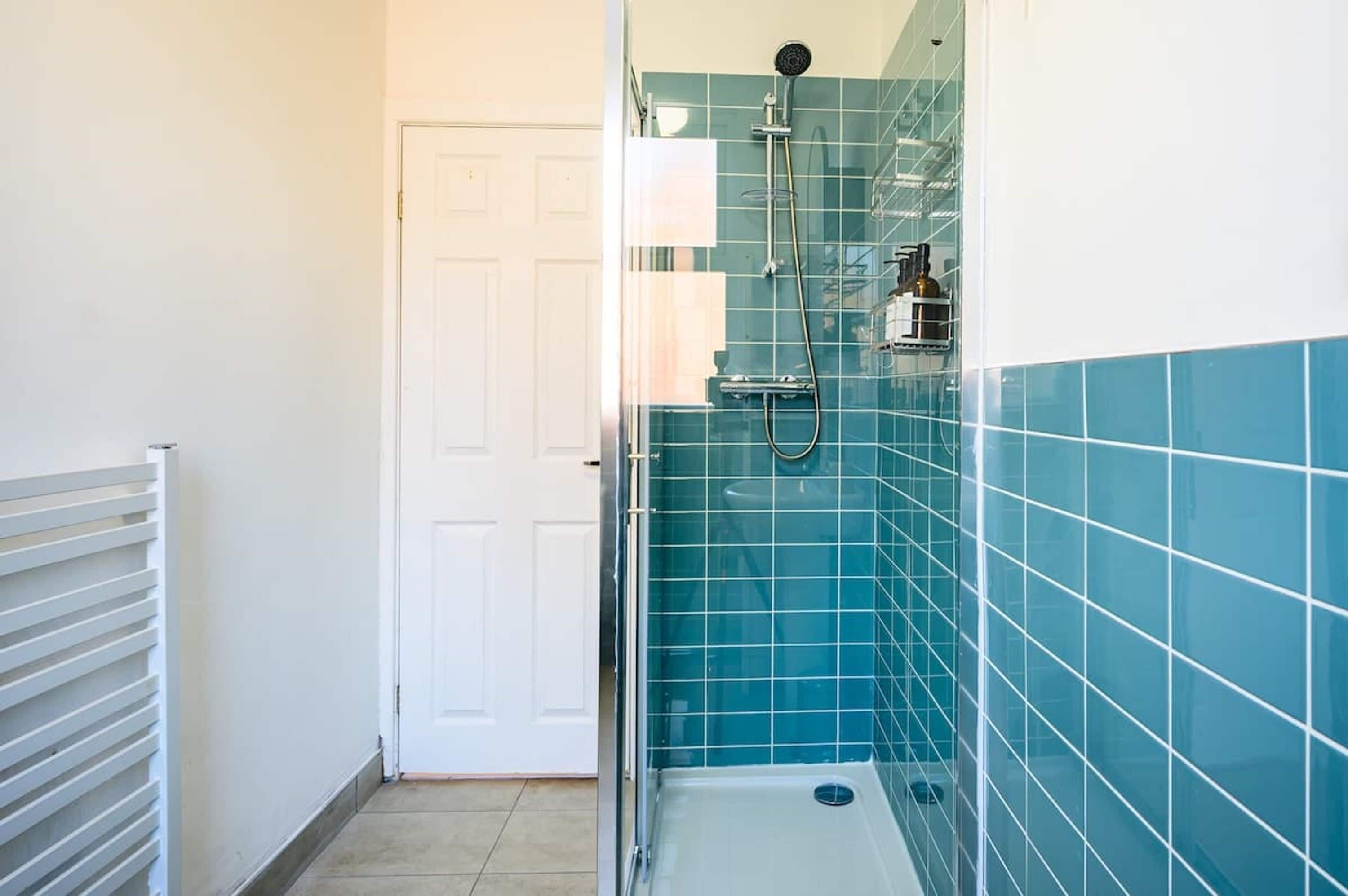 Een badkamer met een douche, een witte deur en blauwe betegelde wanden.