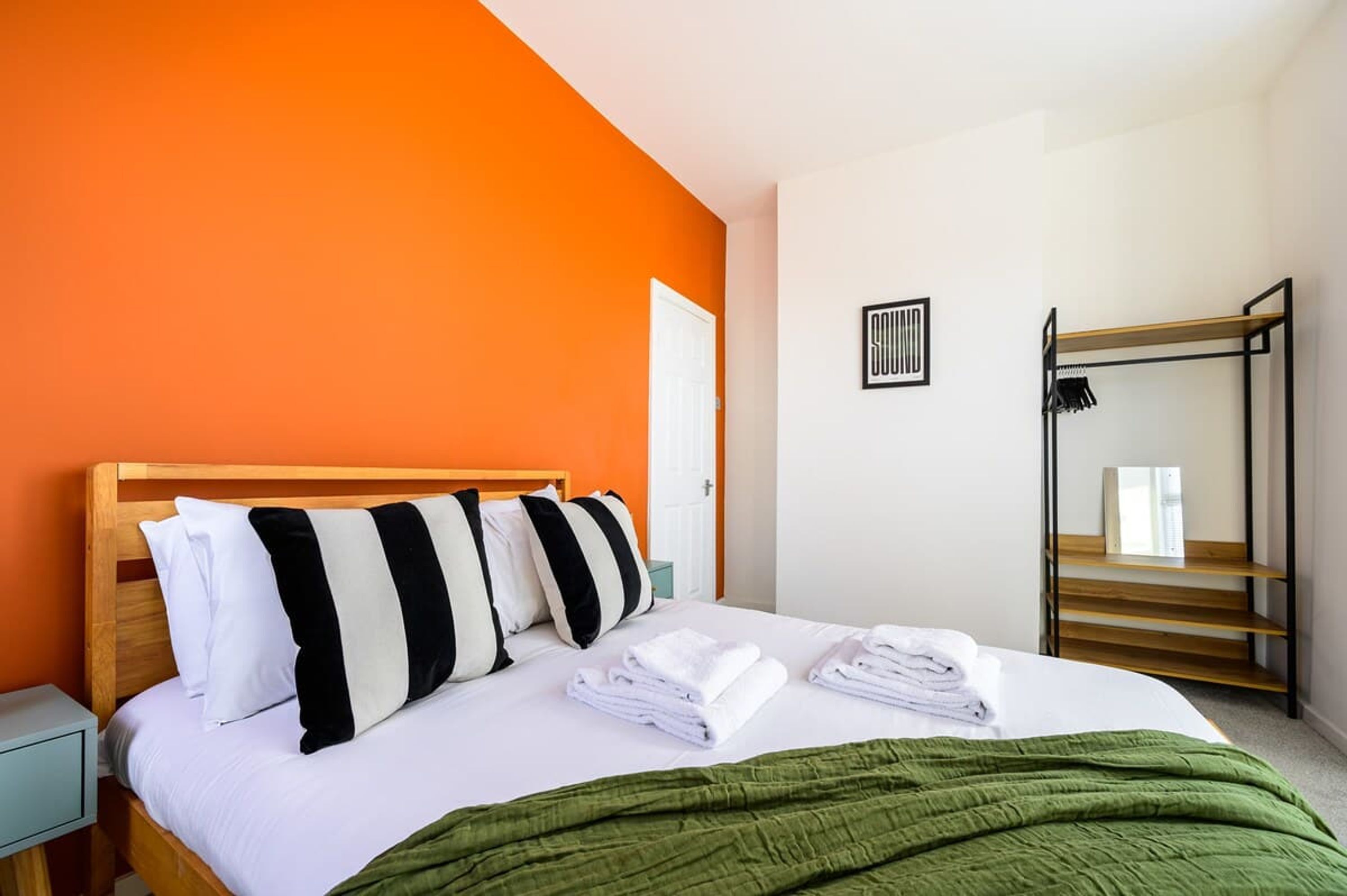 A hotel room with a bed, a green blanket, a wooden headboard, and a white door.