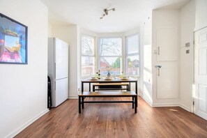 A kitchen with a dining table, a refrigerator, and a bay window with blinds. - Modern 4-bed Free Parking Work Leisure Stays (Manchester)