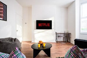 Un salon moderne avec une table basse noire, un fauteuil poire gris et un téléviseur fixé au mur qui affiche le logo « NETFLIX ».