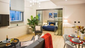Ein modernes Hotelzimmer mit Bett, einer Essecke mit Tisch und Stühlen, einem Fernseher und einem großen Fenster.