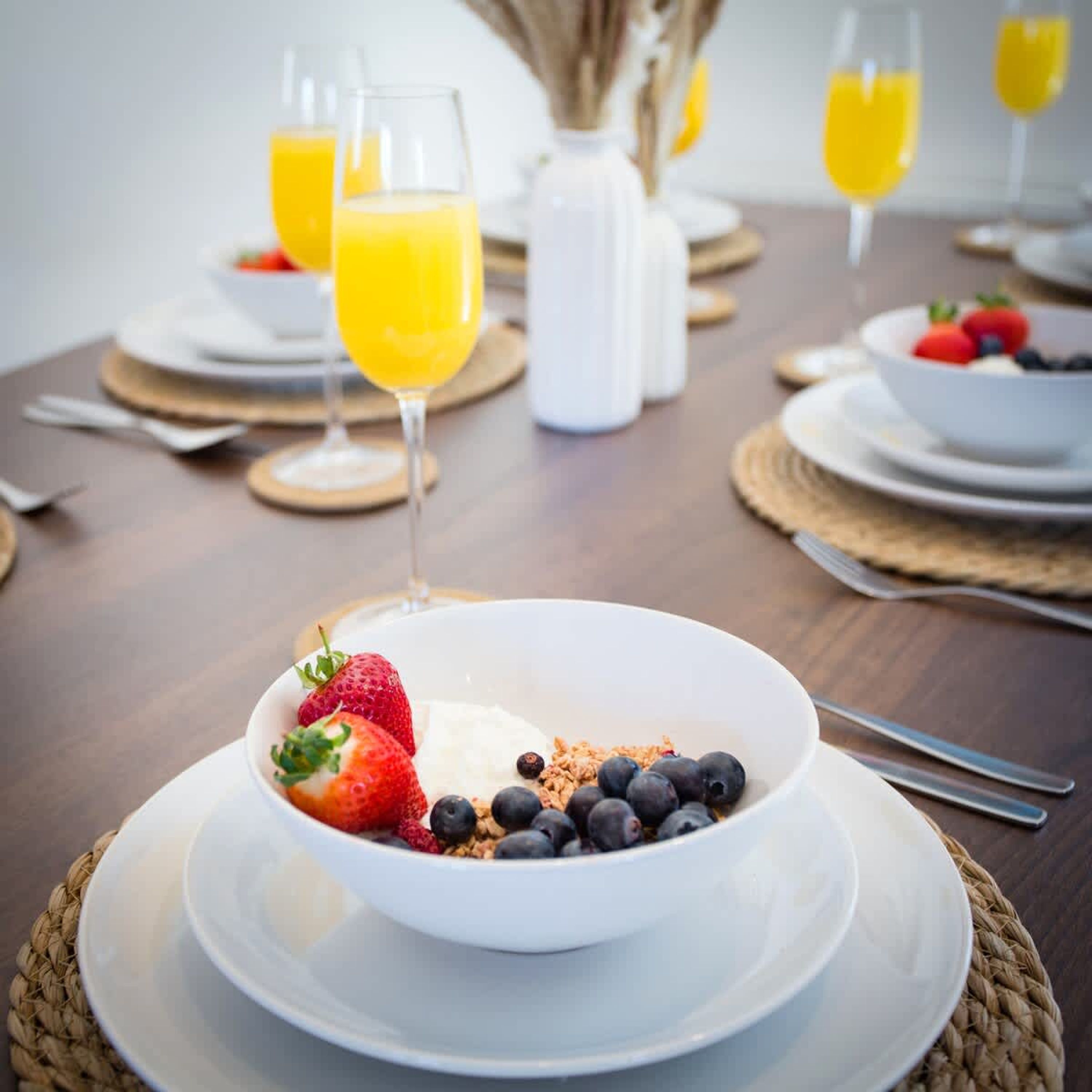 Ein Frühstückstisch mit Joghurt und Beeren, Gläsern Orangensaft und einer weißen Kanne.