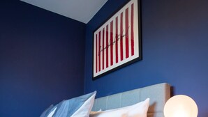 A hotel room with a bed, pillows, a round table with a lamp, and a striped wall art piece. - Comfy 3-bed City Home Parking Near Deansgate (Manchester)