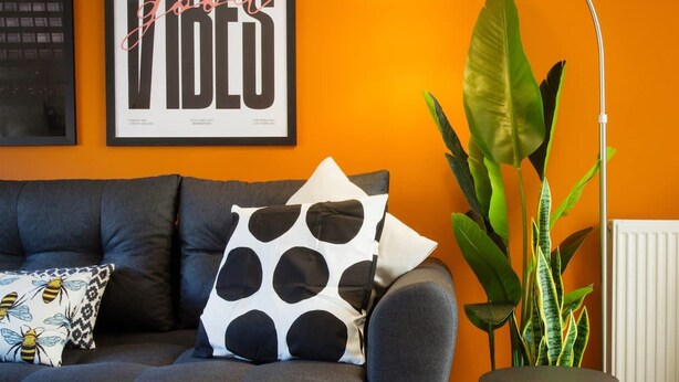 A living room with a sofa, a coffee table with a glass of orange juice, a lamp, and a large plant. - Comfy 3-bed City Home Parking Near Deansgate (Manchester)