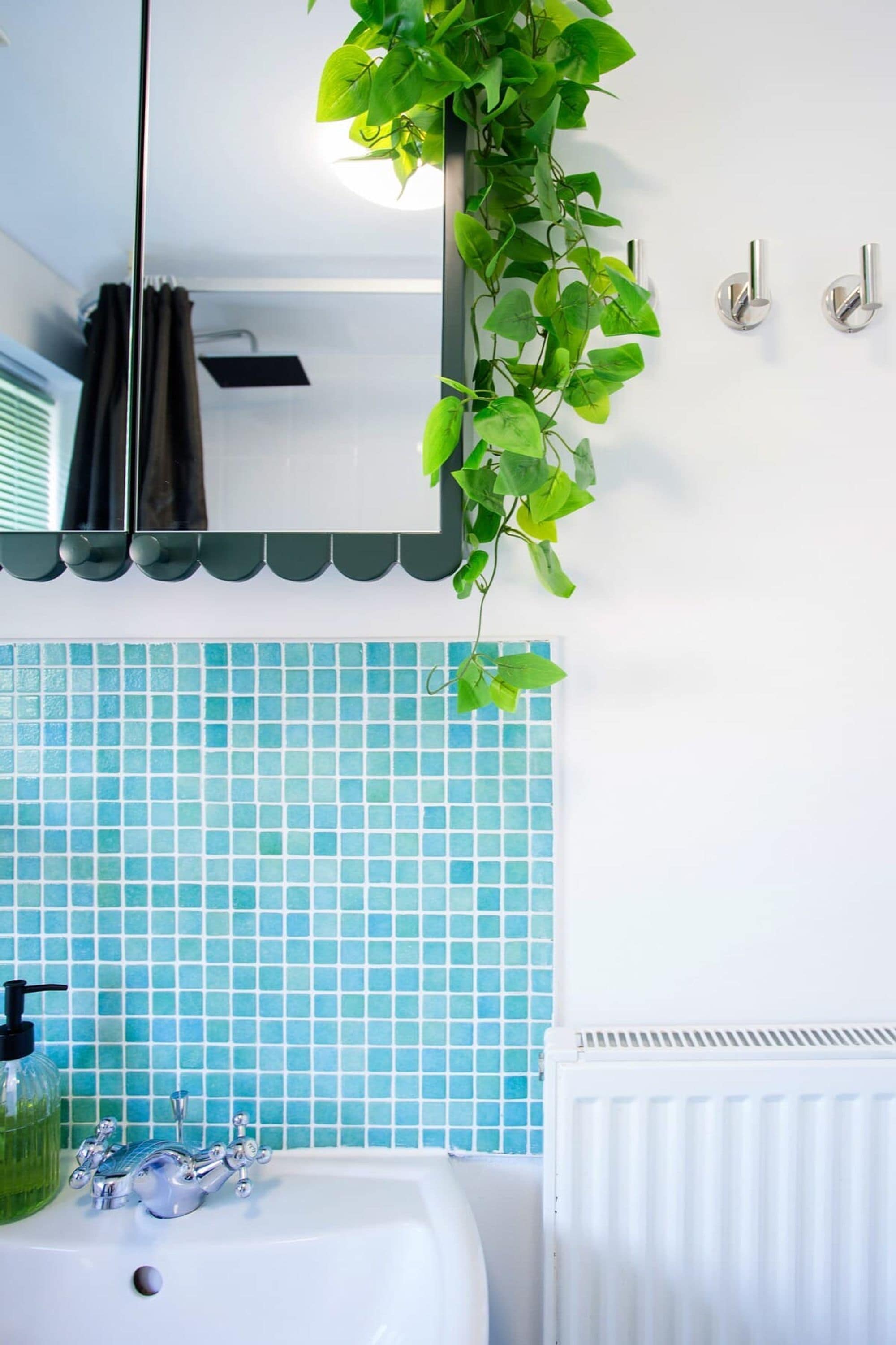 A bathroom with a white sink, blue-tiled wall, a hanging plant, and a mirror.