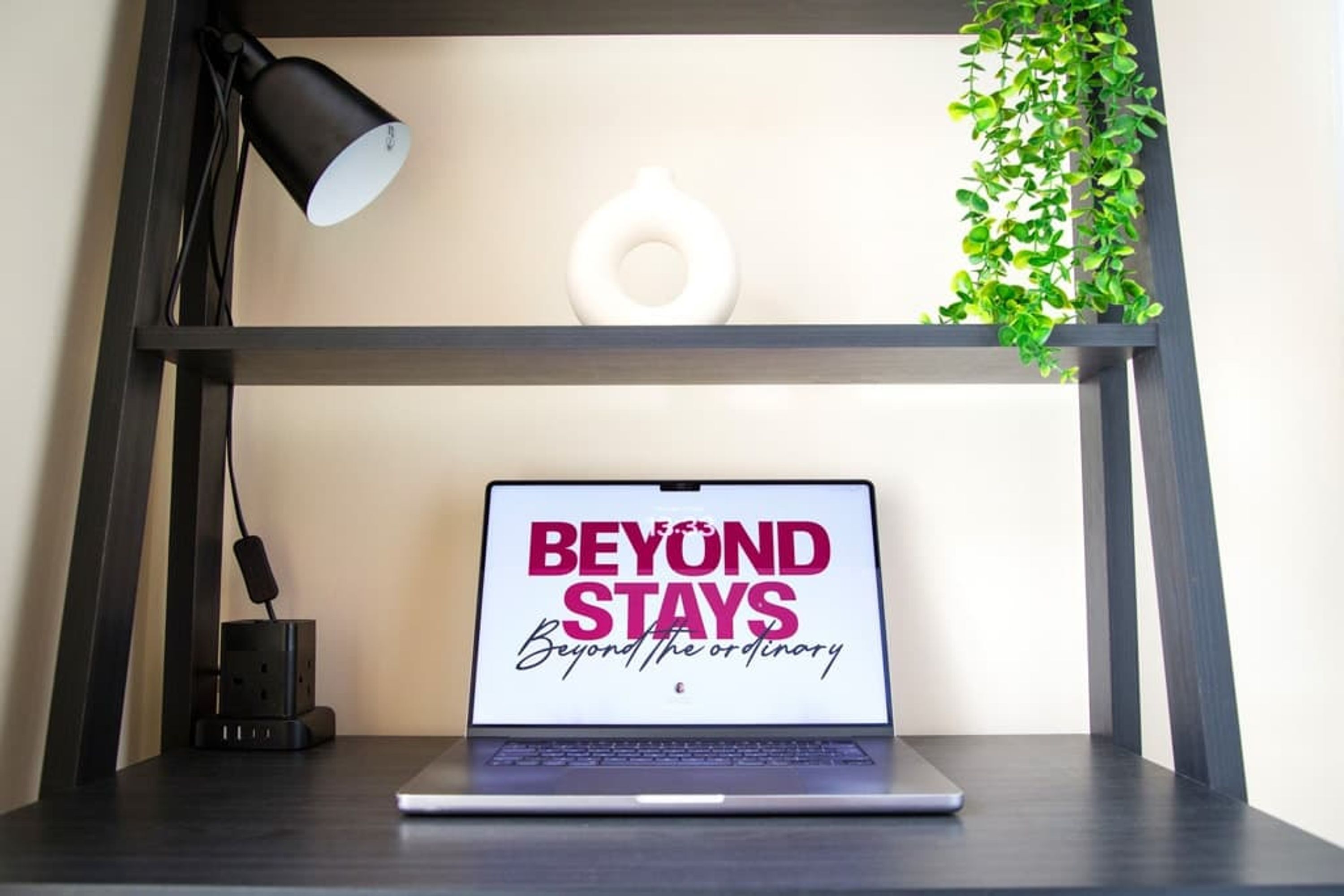 A laptop on a desk with a motivational quote, a power strip, and a hanging plant.