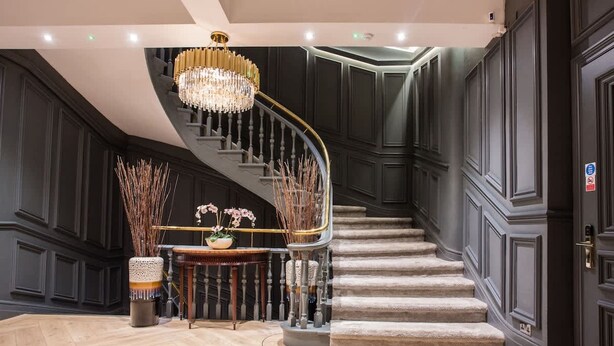 A grand staircase with a chandelier, dark paneling, and a wooden table with a vase of flowers. - Stylish Manchester City Escape Walk to Chinatown (Manchester)