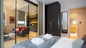 A modern bedroom with a large bed, a dark wardrobe, and a glass door leading to a living area. - Stylish Manchester City Escape Walk to Chinatown (Manchester)