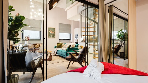 Moderni hotellihuone, jossa on sänky, työpöytä, tuoli, sohva ja portaikko.