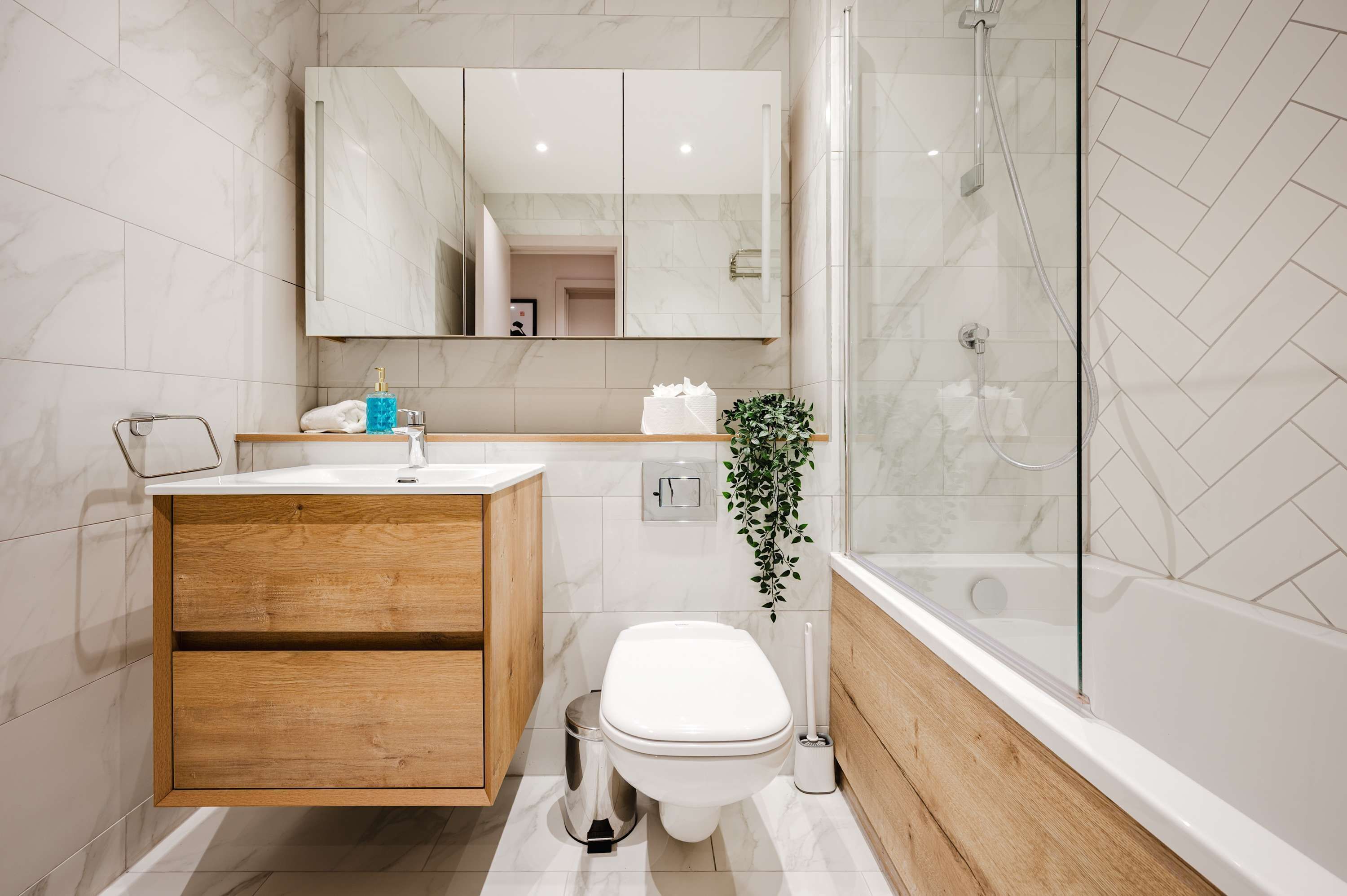 A modern bathroom with a wooden vanity, a white toilet, a glass shower enclosure, and a large mirror.