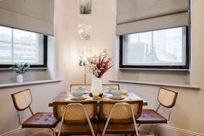 A dining area with a wooden table, wicker chairs, a vase with flowers, and city views through large windows. - Spacious Central Location For Families Walk to All (Manchester)