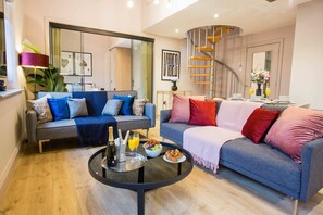 A modern living room with a sofa, coffee table, and a dining area with a spiral staircase. - Spacious 3-bed Retreat Modern Super Central (Manchester)