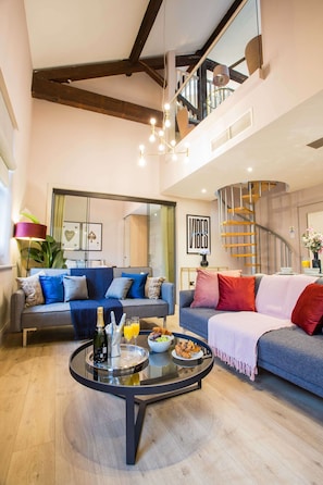 A spacious living area with a modern staircase, a round coffee table with breakfast items, and a sofa with colorful cushions. - Spacious 3-bed Retreat Modern Super Central (Manchester)