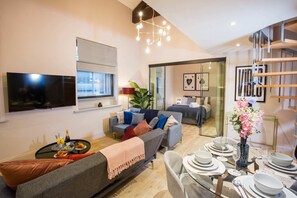 A modern living room with a sofa, a dining table set for four, a TV, and a staircase. - Spacious 3-bed Retreat Modern Super Central (Manchester)