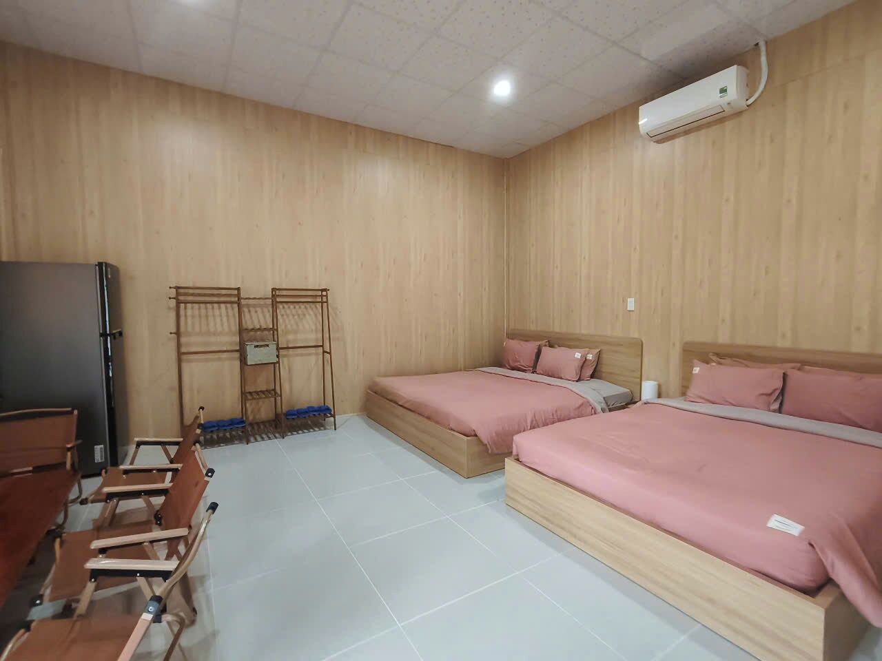 A room with two beds, a desk, chairs, a wardrobe, and an air conditioning unit.