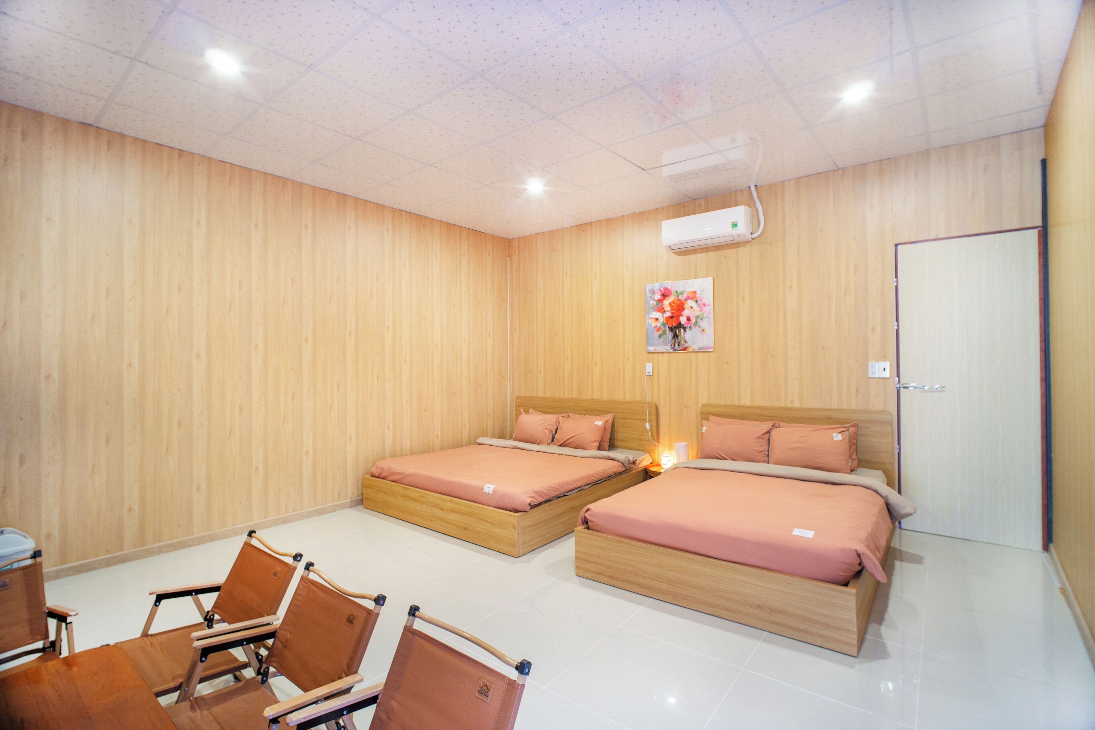 Une chambre d’hôtel avec deux lits en bois, une table à manger avec des chaises et une porte blanche.