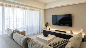 Un salon moderne avec un canapé, une table basse, un téléviseur et une grande fenêtre ornée de rideaux légers.
