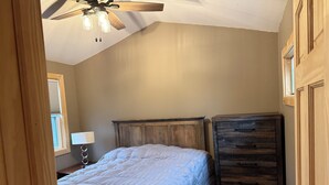 Een slaapkamer met een bed, een dressoir, een plafondventilator en een raam.