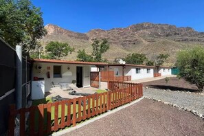 A single-story building with a patio area, a fenced garden, and a mountain backdrop. - Finca Apartment near Maspalomas (Arteara)