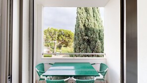 A balcony with a table and chairs, a window with a view of trees and a tall coniferous tree. - 2 bedroom apartment, Vitismar, Vale Parra (Albufeira)