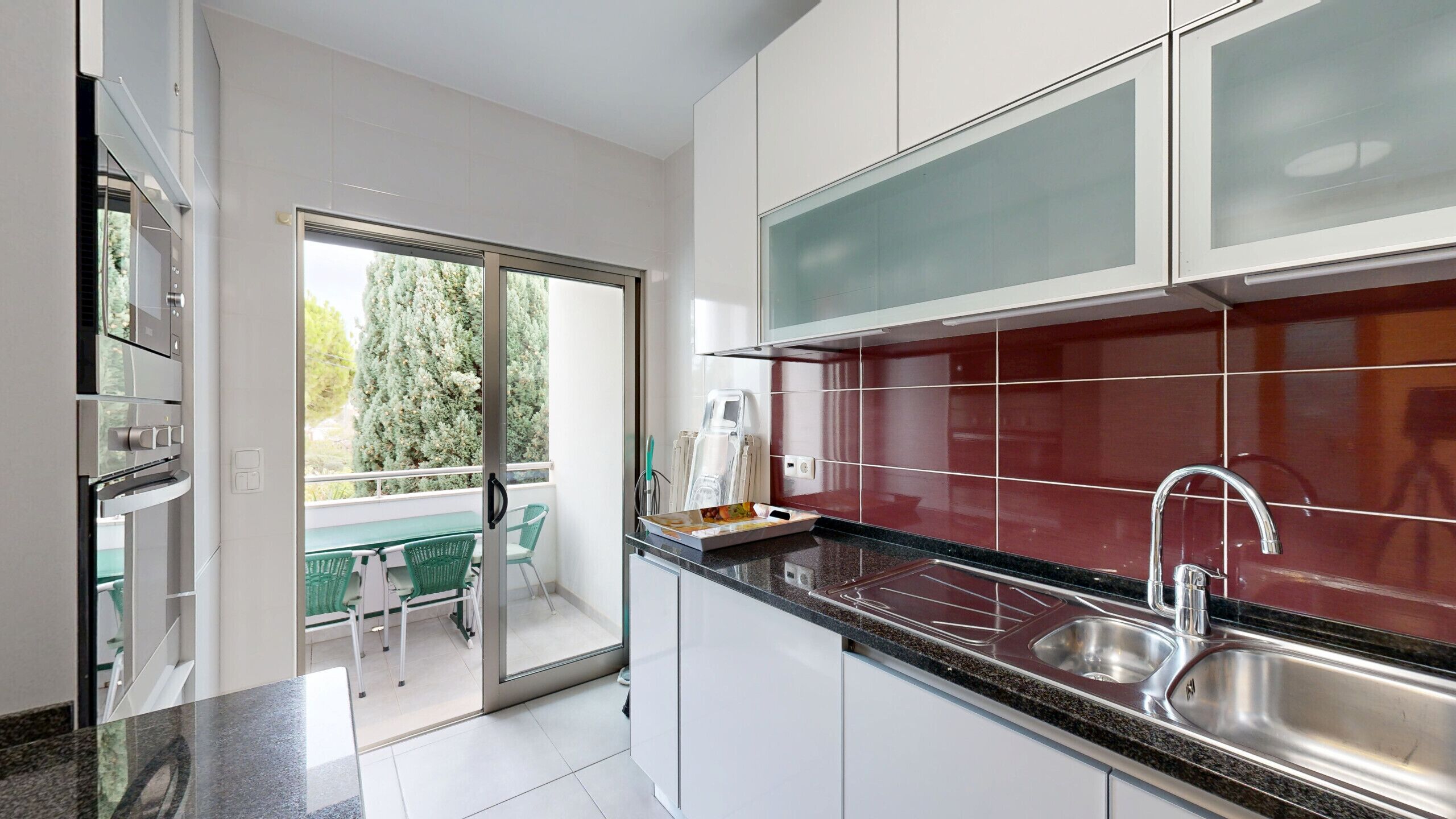 Una cocina moderna con armarios blancos, un salpicadero rojo y un lavamanos de acero inoxidable.