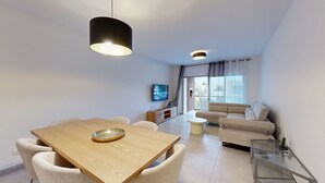 Ein modernes Wohnzimmer mit einer Couch, einem Esstisch mit Stühlen, einem Fernseher und einem Glastisch.
