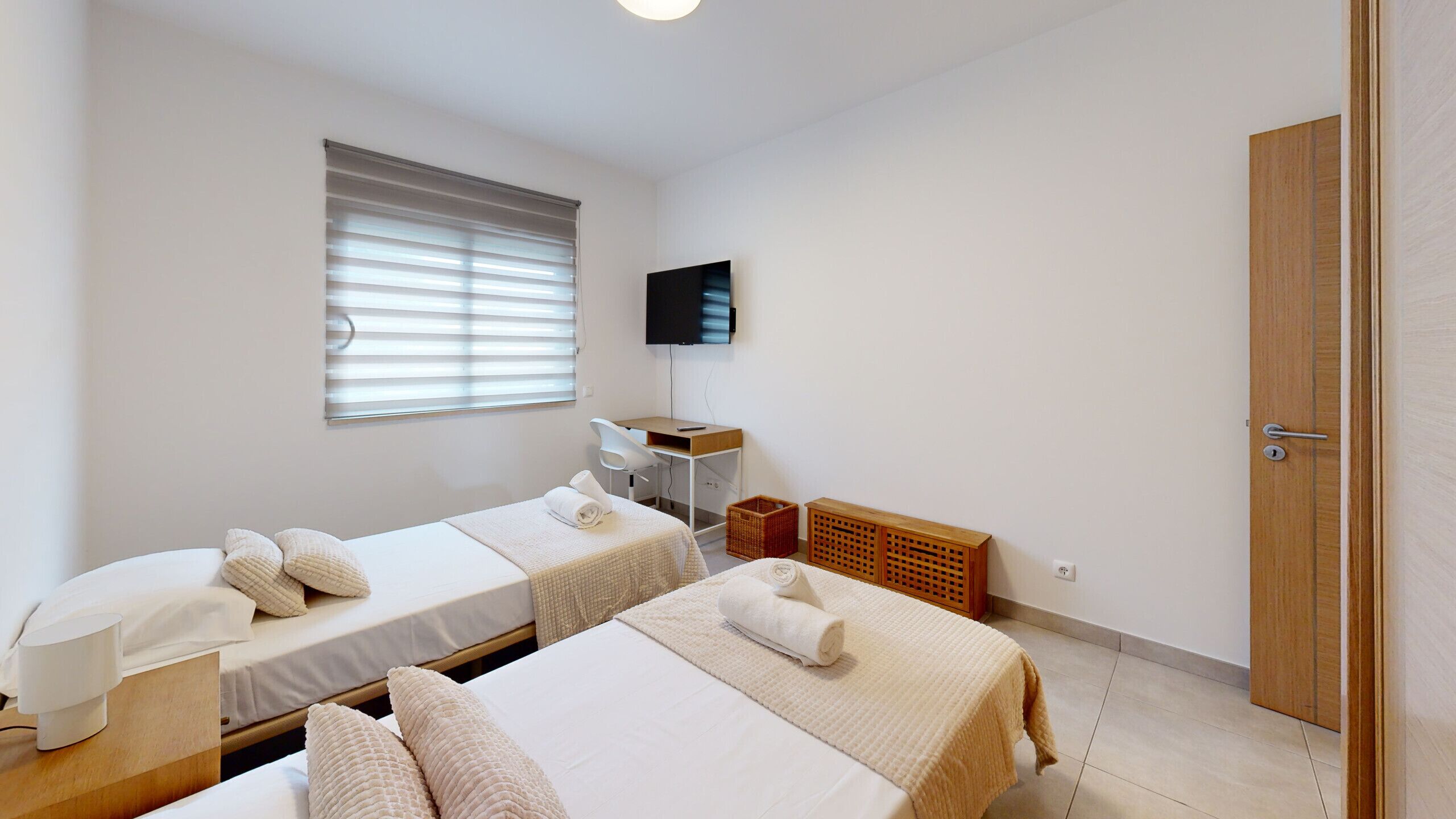 A room with two beds, a desk, a television, and a door.