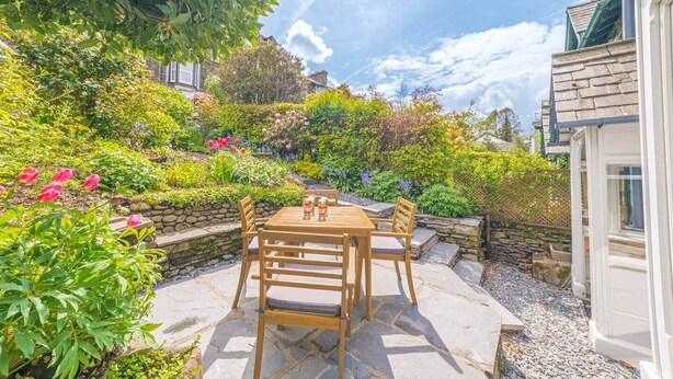 Een terras met een houten tafel en stoelen, omgeven door een tuin met diverse planten en bloemen.