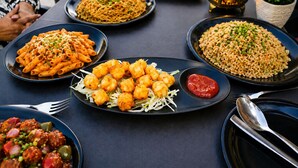 Pöydällä on useita erilaisia ruokia, kuten pastaa, friteerattua kanaa ja riisiä.