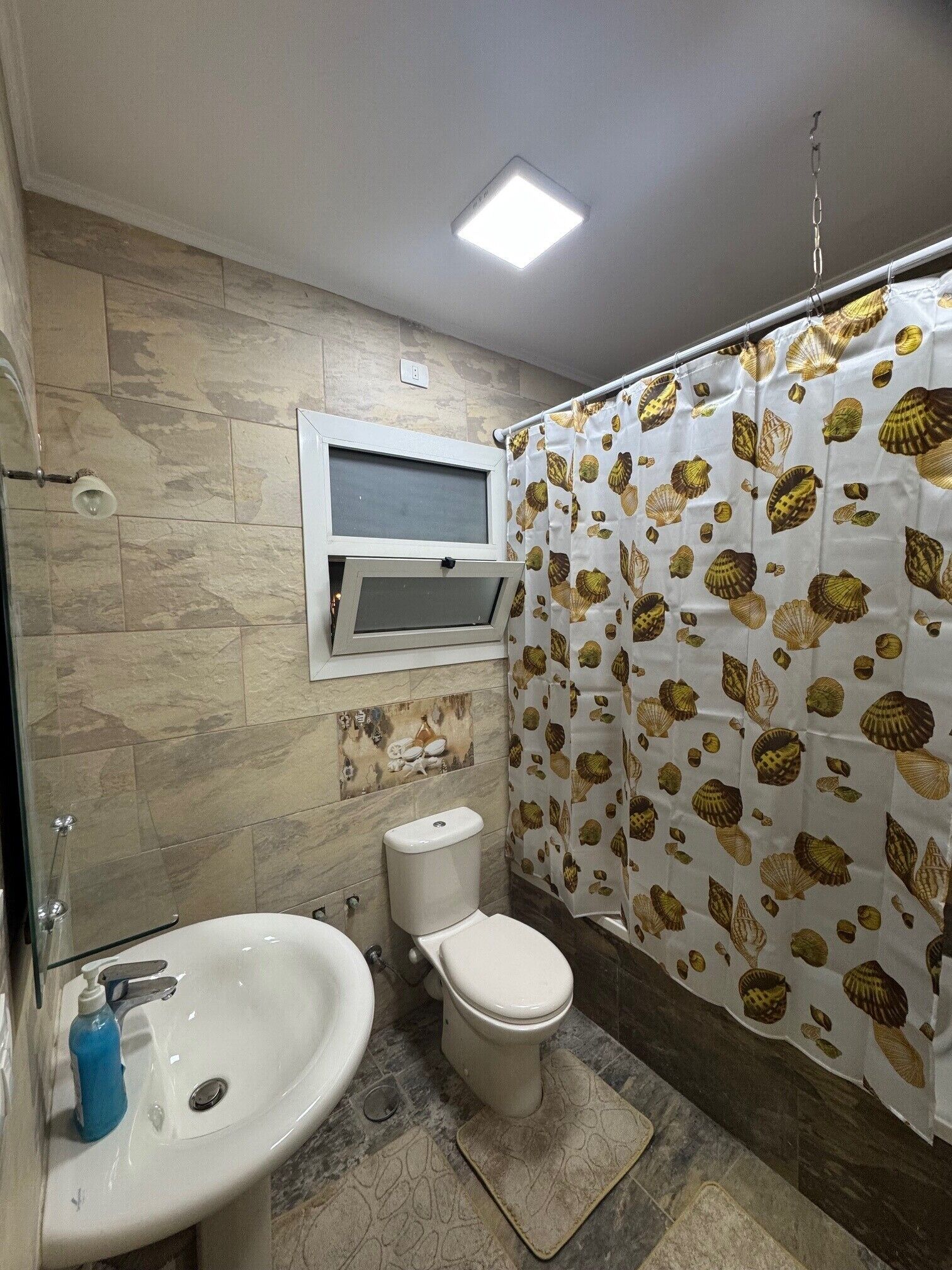 A bathroom with a shower curtain, a toilet, a sink, and a window.