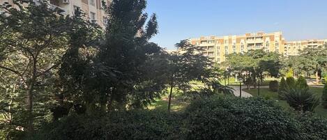 A residential area with a balcony overlooking a courtyard with trees and a building in the background.