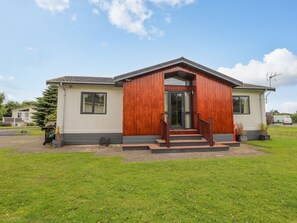 A single-story house with a front porch, a visible garage door, and a well-maintained lawn. - Honeysuckle Lodge (Abergele)