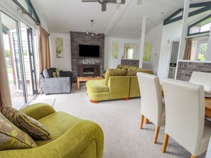 A modern living room with a fireplace, a flat-screen TV, and a dining area. - Honeysuckle Lodge (Abergele)
