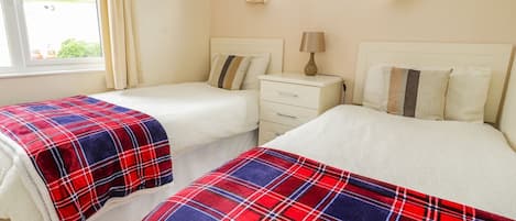 A bedroom with two beds, a bedside table with a lamp, and a window with curtains.