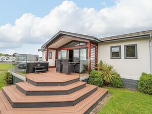A modern mobile home with a deck, outdoor seating, and a garage. - Honeysuckle Lodge (Abergele)