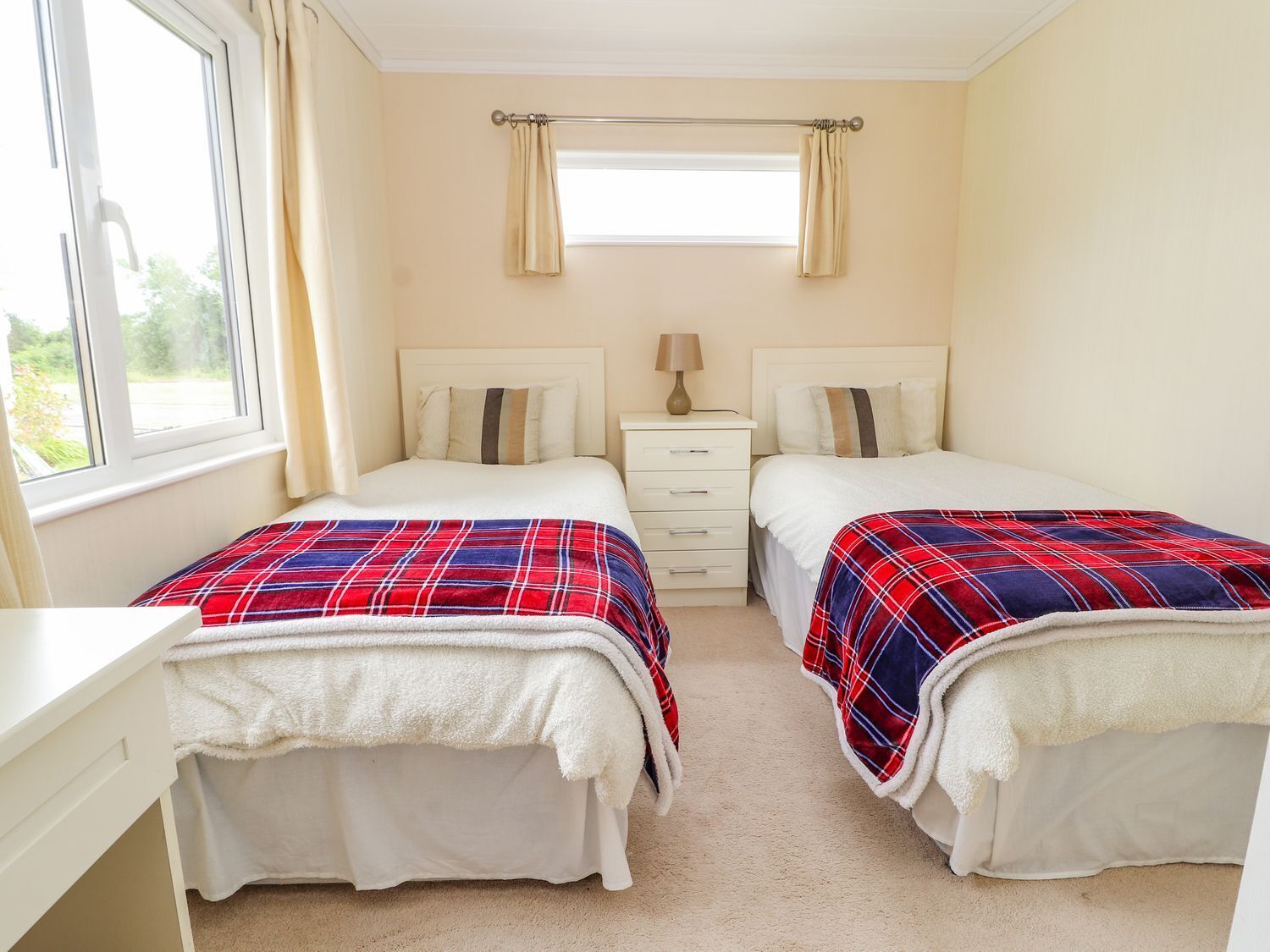 A twin bedroom with two beds, a window, a bedside table, and a nightstand.