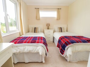 A twin bedroom with two beds, a window, a bedside table, and a nightstand. - Honeysuckle Lodge (Abergele)