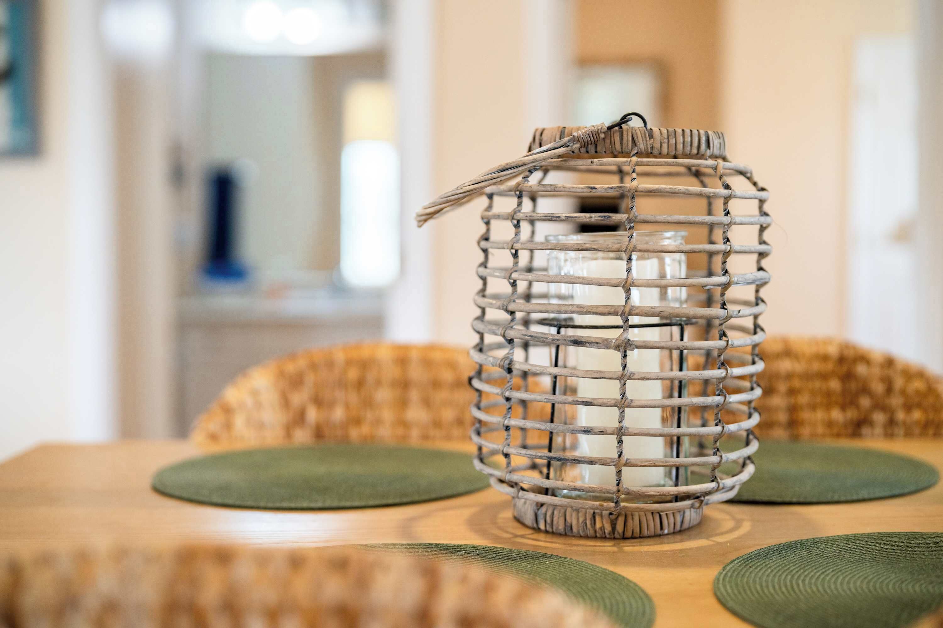 Une lampe en osier, dotée d’un abat-jour en verre, posée sur une table en bois avec des sets de table verts.