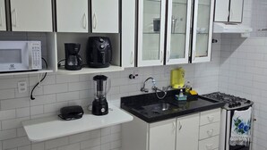 Une cuisine avec des meubles blancs, un four à micro-ondes, une machine à café, un mixeur, un évier et une cuisinière à gaz.