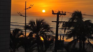 Un coucher de soleil sur l’océan, avec des palmiers et des lignes électriques au premier plan.